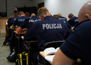 policjanci rozwiązują pisemnie kazus siedząc na krzesłach przy ławkach