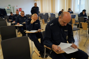 policjanci siedzą na krzesłach, słuchają organizatorów zawodów i przystępują do pisania testu