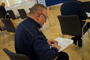 policjanci siedzą na krzesłach, słuchają organizatorów zawodów i przystępują do pisania testu